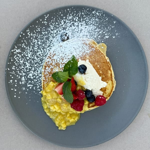 Pancake topped with powdered sugar, berries, mint, whipped cream, and a fruit compote on a gray plate.